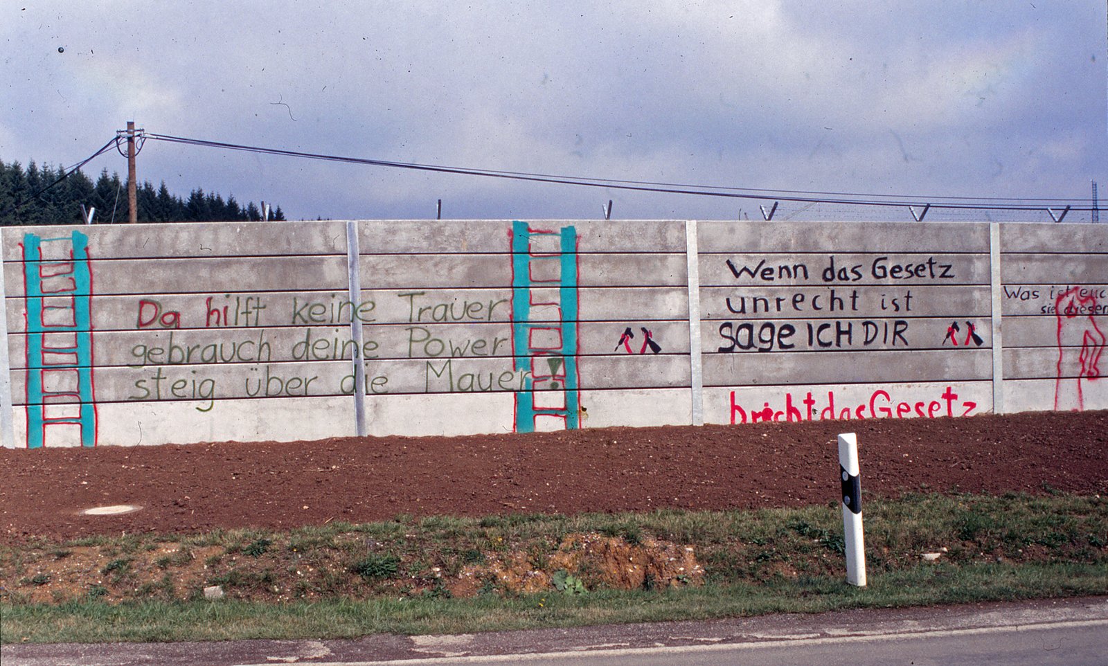 Mauerabschnitt mit aufgemalten Leitern und der Parole über das Übersteigen der Mauer